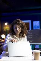 IT expert working from home, opening laptop, testing and deploying programs and systems. Engineer checking code displayed on computer monitors, sitting at desk chair in apartment photo