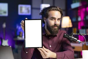 Tech engineer presenting isolated screen tablet in entry level low budget price range, filming from dimly lit home studio. Content creator reviewing mockup digital device in front of online audience photo
