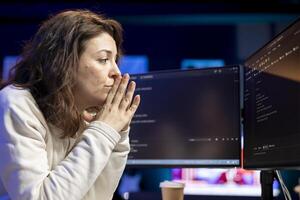 Pensive woman developing software in Java programming language using desktop PC, examining. Contemplative programmer in apartment thinking how to solve coding issues on computer photo