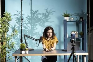 Content creator using mic in studio to do ASMR , discussing with viewers using soothing voice. Woman using professional microphone and smartphone to record podcast with crisp sound photo