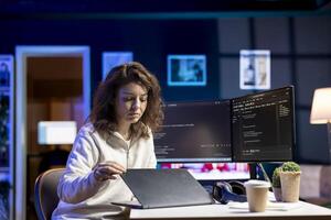 Cybersecurity specialist using laptop to look for company security vulnerabilities, comparing with computer monitors. Developer installing fortified code on laptop, crosschecking with PC screens photo