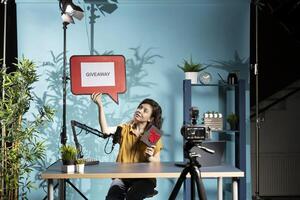 Vlogger advertising giveaway for audience with cardboard sign, holding gift box, explaining how to win prize. Person using copy space board to inform her internet community about contest photo