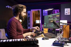 Male composer producing sounds and mixing them on stereo console, creating modern cool soundtracks in his home studio. Young artist songwriter adjusting volume levels in post production. photo