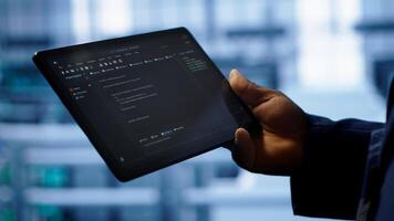 Programmer monitoring server room rigs, doing checkup, inputting data on tablet of needed fixes. IT specialist working in data center facility housing storage hardware, camera A close up photo