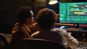 Music production team examining volume levels on audio software, using mixing and mastering techniques to create a hit song. Musician and sound designer work on editing recorded tracks. Camera A. photo