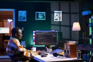 Programmer in home office concentrating on finding bugs while he codes on his computer. African american IT admin frowning while looking at screen, confused by errors in lines of code. photo