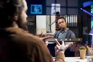 IT admin working from home in videocall with african american coworker, testing programs and systems. Programmer checking code with colleague in online teleconference, sitting at desk in apartment photo