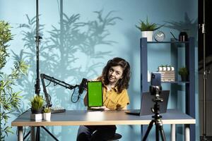 Tech engineer presenting isolated screen tablet in entry level low budget price range, filming from dimly lit home studio. Content creator reviewing mockup digital device in front of online audience photo