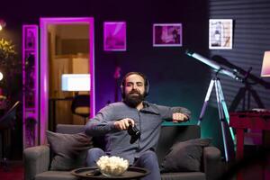Man taking break after playing videogames in apartment all day, setting controller down. Gamer taking time out from participating in PvP online multiplayer game using console system photo