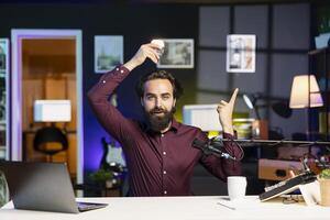 Content creator using light bulb to illustrate idea, having brilliant insight to tell audience. Entertainer pointing finger up to show inspiration concept while filming in apartment photo