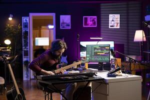Sound engineer recording his acoustic guitar accords in home studio, working on mixing and mastering music. Artist using professional editing and composing gear, post production. photo