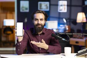 Portrait of smiling tech expert assessing mockup cellphone performance, talking about parts used inside. Entertainer unboxing isolated screen mobile phone to review it on technology internet channel photo