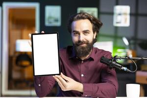 Portrait of smiling man in studio filming mockup tablet review for tech enthusiasts. Cheerful online star hosts technology internet show, unboxing isolated screen digital portable device photo