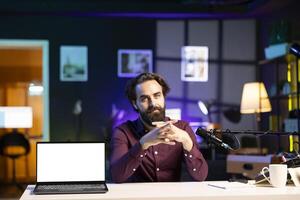 Man doing live broadcast talking to audience about recent news headlines, reading from mockup laptop. Online show host talking with subscribers, presenting information from isolated screen notebook photo