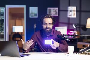 Portrait of happy reviewer discussing with viewers about mini led lights during live broadcast on internet. Cheerful influencer talking with fans during stream, filming RGB lighting device in studio photo