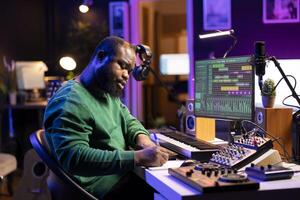 Talented artist composing new lyrics for his tracks and recording music with audio devices in his home studio. Singer composer writes melodic material by taking notes and creating rhymes or songs. photo