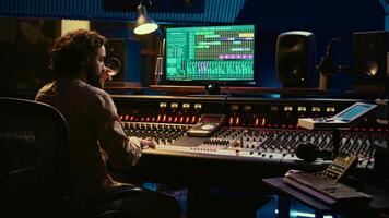 Audio technician uses mixing and mastering techniques in studio to edit and process tracks, working on console with moving faders and colored meters. Sound designer removing white noise. Camera B. photo