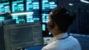 Data center computer scientist wearing mic headset, doing installation of networking equipment. Server hub IT professional talking in microphone with system administrators, camera A photo