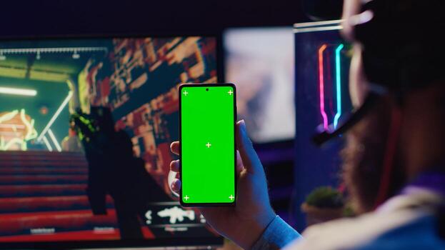 Man watching favorite content creator on green screen smartphone showing tips for game he is currently playing, close up. Player looking online for inspiration on chroma key phone, stuck on mission photo