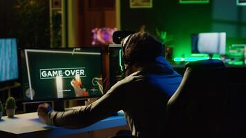 Angry man frustrated after losing science fiction FPS videogame level in RGB lit apartment late at night. Upset gamer raging, punching table after failing in online multiplayer shooter photo