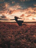 A woman joyfully leaps in a vibrant field during a stunning sunset. photo
