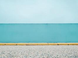 A minimalist scene featuring a blue wall against a gravel surface and a yellow curb. photo