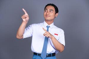 Indonesian Male High School Student in Uniform Smiling While Pointing Finger Isolated Background photo