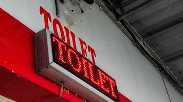 Bright red LED sign displaying 'TOILET' on a wall with a matching painted label. The image captures a modern restroom indicator in a public space, highlighting clear signage and direction. photo