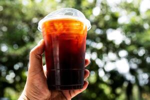 Man holding a take out iced black coffee with nature bokeh background photo