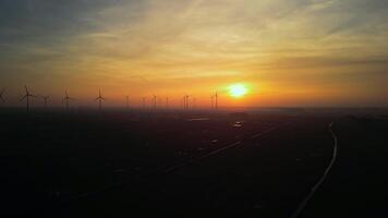 row of wind turbines are lined up in a field, with the sun setting in the background. Concept of energy and progress, as the turbines harness the power of the wind to generate electricity video