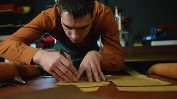 Craftsman intently tracing patterns onto leather sheets, showcasing precision and craftsmanship in the early stages of leather goods creation video