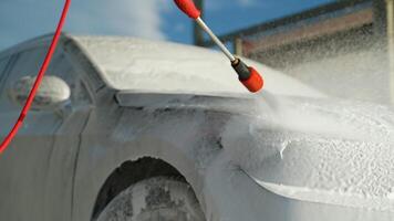 A man using a red pressure washer to cover his car in foam at an outdoor self-service car wash video