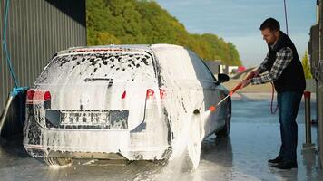 A man spraying foam on a car with a red pressure washer video