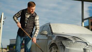 A man using a mop to clean his car at an outdoor self-service car wash video