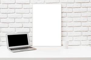 Workspace featuring a laptop and a blank canvas on a minimalist desk against a brick wall photo
