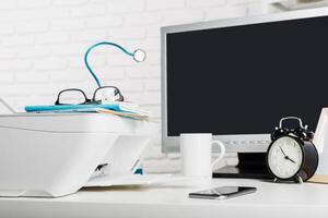 Office workspace with printer, computer, and personal items in a clean environment during daytime photo