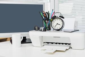 Office workspace with printer, computer, and clock showing morning routine setup in a bright environment photo