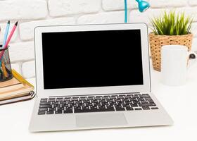 Modern workspace with a laptop, stationery, and greenery during daytime photo