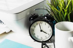 Clock placed on a desk beside a plant, printer, and mug in a workspace filled with productivity elements photo