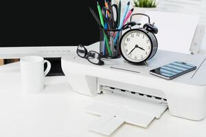 Workspace setup with printer, alarm clock, stationery and coffee cup on a clean table photo