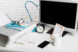 Workspace setup with printer, computer monitor, clock, and accessories on a desk during daylight photo