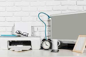 Desk workspace featuring a printer, clock, monitor, and office supplies in a modern setting photo
