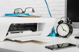 Printer on desk with glasses, clock, notebook, and smartphone at workspace during daytime photo