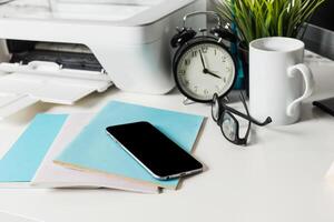 Work desk setup with a phone, clock, and notebooks during daytime in a home office photo
