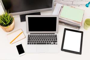 Workspace setup with laptop, tablet, smartphone, and office supplies in a bright environment photo