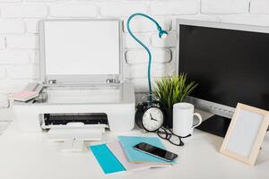 Desk setup featuring printer, clock, computer, and personal items in a modern workspace photo