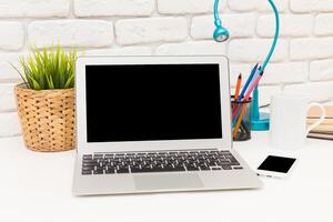 Modern workspace with laptop, stationery, and plants on a desk in a bright and inviting environment photo
