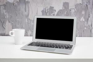 Modern workspace with laptop and coffee cup on minimalistic table against a textured wall backdrop photo