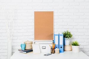Desk workspace setup featuring a corkboard, stationery, and plants in a bright room during daylight photo
