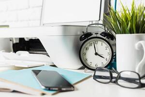 Clock and office supplies on a workspace with modern technology and greenery indicating a productive environment photo